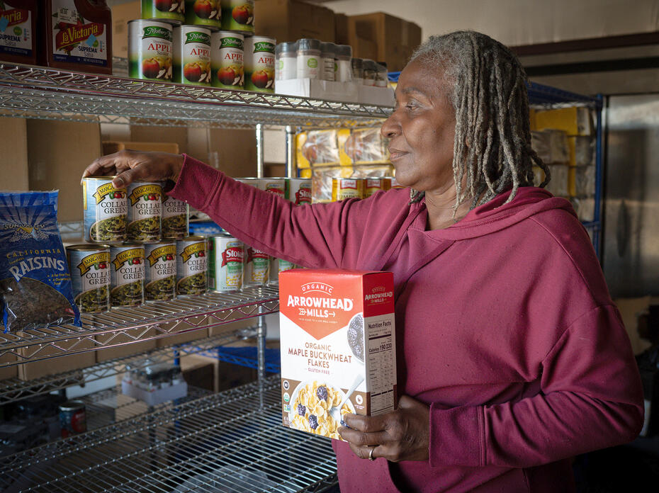 A woman puts nonperishable food on pantry shelves.