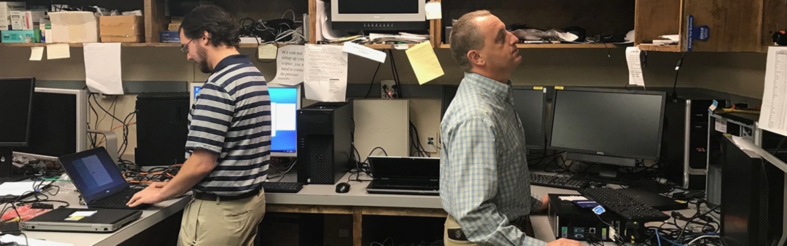 Two men in a computer lab facing opposite one another working on computers