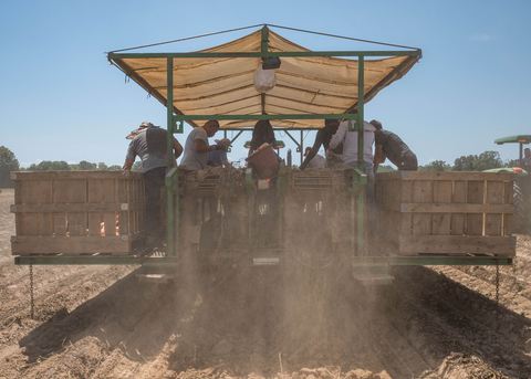 Seven people work on a trailer pulled through a dusty field.