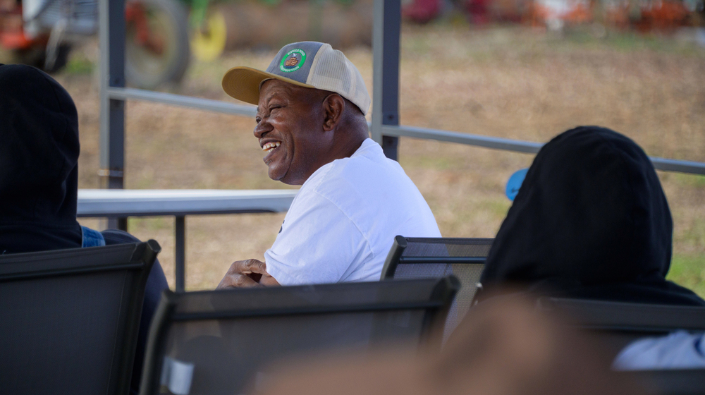 A seated man wearing a baseball hat and smiling.