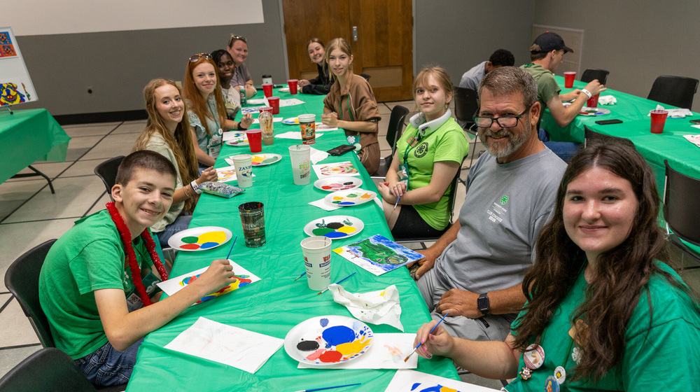 Teens smiling with an adult at a table full of painting supplies.